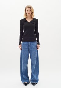 Maglietta nera a maniche lunghe con scolla a V a coste, abbinata a jeans blu in denim oversize e tacchi a punta neri. Silhouette semplice e strutturata.