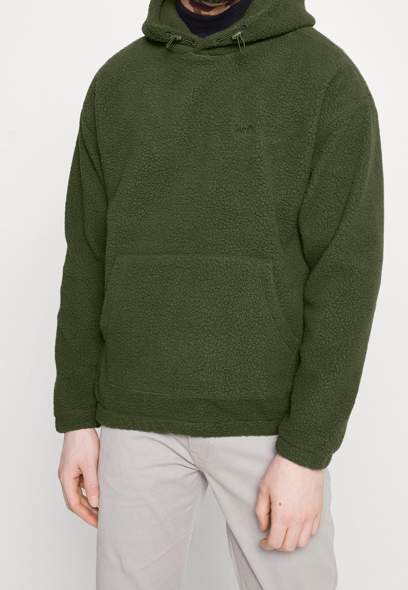 Felpa con cappuccio color verde oliva in pile con superficie testurizzata, tasca frontale e cappuccio con coulisse regolabile. Presenta un logo discreto sul petto.