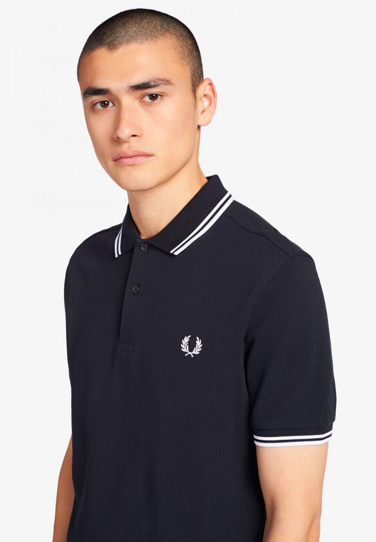Polo di colore navy realizzato in cotone testurizzato, con una patta a due bottoni, accenti a righe bianche sul colletto e sulle maniche, e un logo sul petto.
