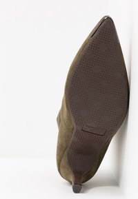 Chaussure en suède marron à bout pointu avec semelle en caoutchouc texturée, petit talon et logo "xti" sous la semelle.