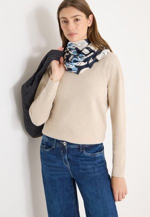 Pull beige, jean foncé et écharpe à motif avec des accents bleus. Tient une doudoune noire, avec une texture lisse et une coupe décontractée.