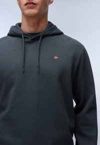 Donkergrijze hoodie met een kangoeroezak, koordjes en een kleine geborduurde Noorse vlag op de borst. Gemaakt van een zachte katoenen mengeling.