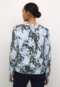 Lange mouwen blouse in lichtblauw met een donkergrijze abstracte patroon. Heeft een ronde halslijn en knoopmanchetten. Soepele stofstructuur.