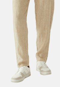 Bílé a béžové sneakers s měkkou texturou, s vrstveným designem a gumovou podešví, spárované se světle béžovými lněnými kalhotami.