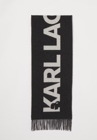Sort tørklæde med store hvide bogstaver, der staver "KARL LAGERFELD." Lavet af et blødt materiale med frynse-detaljer i enderne.
