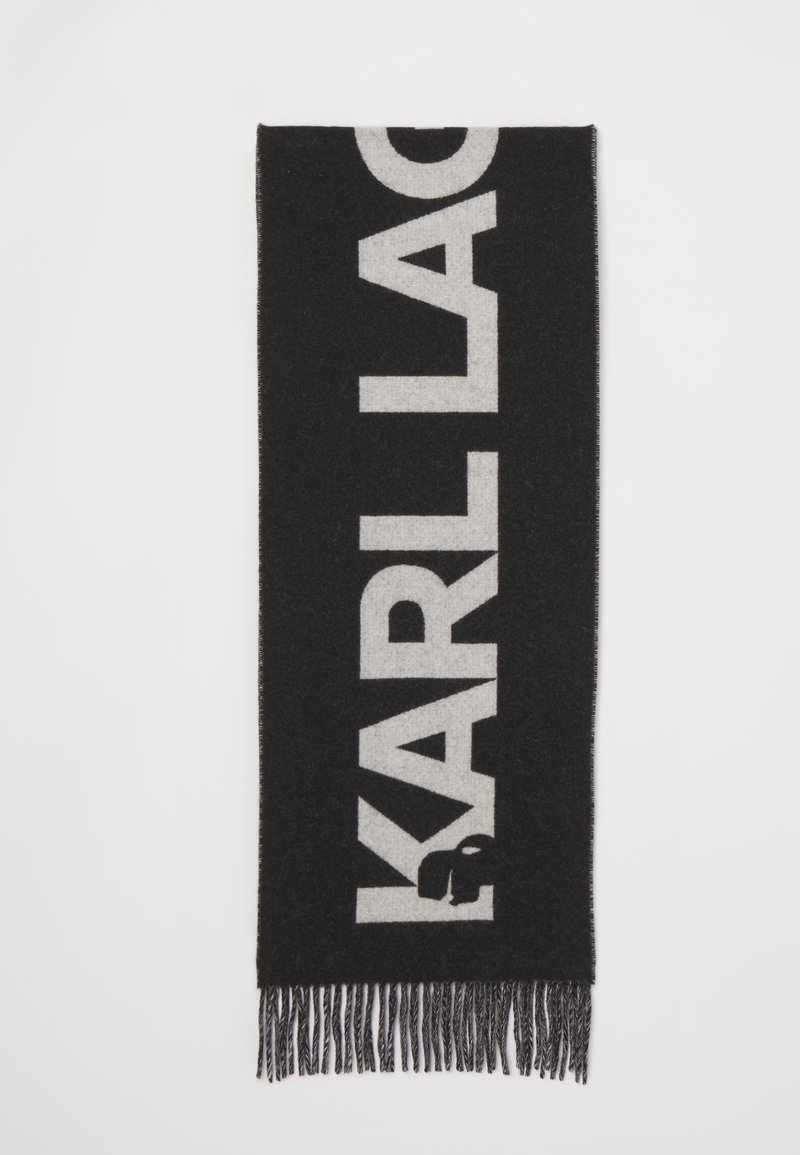 Sort tørklæde med store hvide bogstaver, der staver "KARL LAGERFELD." Lavet af et blødt materiale med frynse-detaljer i enderne.