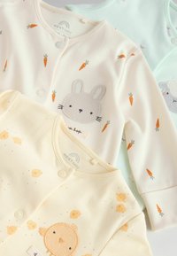 Tre babyplagg: ett krämfärgat med morotsmönster och kaninbroderi, ett ljusgult med kycklingmotiv, och ett mintgrönt med får.