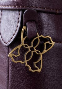 Dark burgundy leather bag with a smooth texture, featuring a brass butterfly-shaped accent attached to a leather strap.