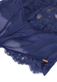 Navy blauw doorschijnende mesh en kanten lingerie met golvende randen, voorzien van bloemenpatronen en een klein gouden hardware detail.