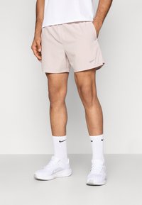 Heledad valge atletikapüksid, mis on valmistatud kergest kangast, küljetaskudega ja väikese hõbedase Nike logoga. Kandmisega kaasas valged Nike jalanõud ja sokid.