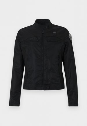 Crna jakna na patentni zatvarač s visokim ovratnikom, kopčama na drukere, džepovima na prsima sa zatvaračima i zakrpa na gornjem lijevom rukavu.