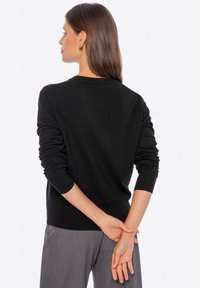 Maglione nero lavorato a maglia con maniche lunghe, scollatura a girocollo, vestibilità casual e polsini e orlo a coste, abbinato a pantaloni grigi.