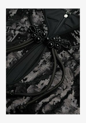 Tissu noir en sequins avec une fermeture éclair, accentué par des nœuds et des liens en perles noires. Texture lisse avec des détails complexes en perles.