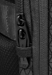 Dettaglio di cerniera nera su una superficie di tessuto strutturato, con due tiretti e una cinghia intrecciata per una presa e una durata maggiori.