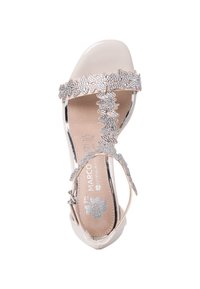 Beige sandal with a clear strap, embellished silver leaf motif, ankle buckle, and a cushioned footbed. Smooth texture and open toe design.