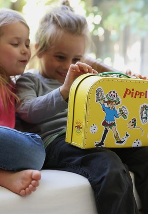 Due bambini seduti su un divano che esaminano una scatola pranzo gialla a tema Pippi Calzelunghe con adesivi colorati dei personaggi.