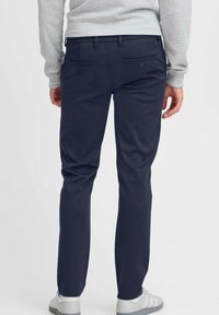 Chinos azul marino con corte recto, que cuentan con dos bolsillos traseros con botones y presillas para cinturón, combinados con un sudadera gris claro y zapatillas.