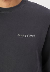 Sudadera de manga larga gris oscuro con un cuello redondo. Presenta el logo bordado "LYLE & SCOTT" en blanco en el área del pecho izquierdo. Textura suave.