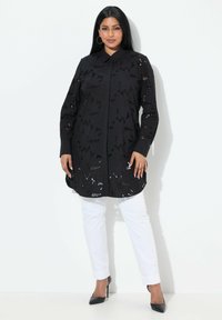 Tunica nera a maniche lunghe con ritagli floreali, con colletto, abbinata a pantaloni bianchi e tacchi neri; tessuto liscio, vestibilità slim.