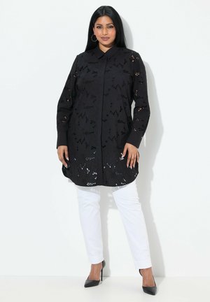 Túnica negra de manga larga con recortes florales, con cuello, combinada con pantalones blancos y tacones negros; textura suave, ajuste entallado.