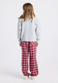 Un pull en laine gris et un pantalon de détente à carreaux rouges, avec une coupe ample et une taille élastique, portés avec des chaussures de couleur crème.