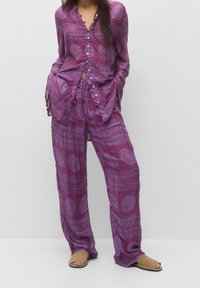 Paarse button-up top met bijpassende losse broek, voorzien van een cirkelpatroon en een gladde textuur. Draag het met tan open-toe sandalen.