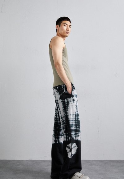 Un top verde măsliniu ajustat asociat cu pantaloni largi alb și negru cu imprimeu tie-dye, având un model unic și un detaliu rotund pe piciorul stâng.