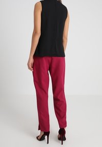 Svart ärmlös topp med en slät textur, i kombination med fuchsia byxor med rak passform och sidöppningar. Svarta högklackade skor.