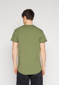 Oliven grønn kortermet t-skjorte med rund halslinning og rullede ermer. Stoffet ser mykt og glatt ut med en avslappet passform.