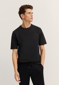 Czarny bawełniany t-shirt z okrągłym dekoltem i krótkimi rękawami. Posiada subtelne logo z przodu. Gładka tekstura i swobodne dopasowanie.