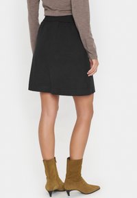 Jupe noire à taille ajustée, au design évasé et à la texture lisse. Associée à des bottes chelsea en suede marron avec un petit talon.