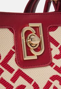 Sac à main en cuir rouge avec une base tissée crème ornée d'un motif rouge vif. Le fermoir est souligné par une quincaillerie dorée avec un détail de logo.