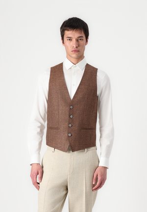 Gilet en tweed marron avec une finition texturée, six boutons à l'avant, deux poches, porté sur une chemise blanche et un pantalon clair.