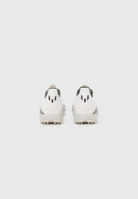 White athletic shoes feature a smooth design with black accents, a textured heel, and a low profile for stability. Cleats visible on the sole.
