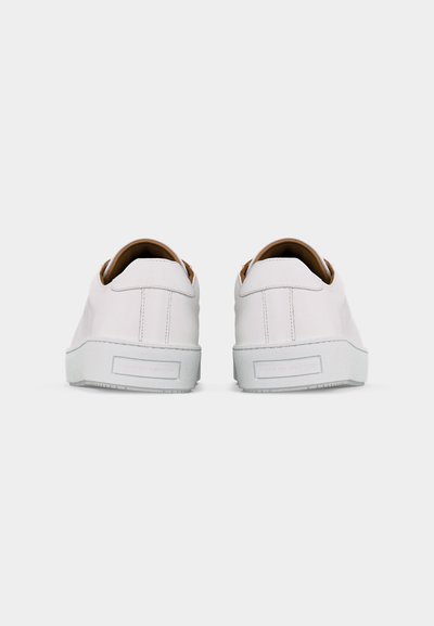 Porą baltų žemų sportinių batų su odinėmis viršutinėmis dalimis, matomas iš nugaros, ant paprasto šviesiai pilkos spalvos fono.