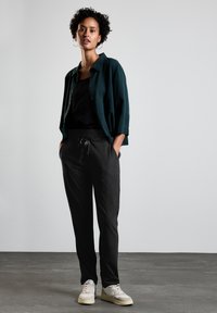 Tmavě zelená oversized košile, černý top a šedé žebrované tepláky s šňůrkou, doplněné krémovými teniskami; hladké materiály a volný střih.