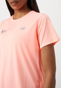 T-shirt de sport rose à manches courtes en tissu texturé et respirant. Présente un logo argenté sur la poitrine et un col rond.