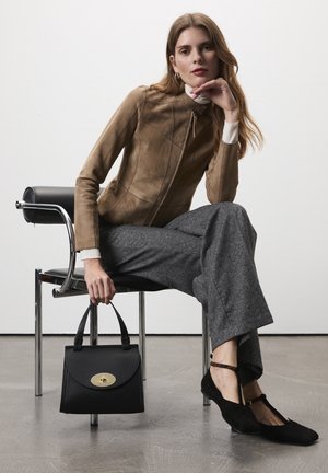 Veste en cuir tan au design ajusté, pantalon large gris, sac à main structuré noir et chaussures en daim noir avec des brides de cheville.