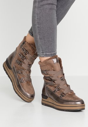 Ben i grå jeans iført brune vinterstøvler i ruskind og læder med tykke såler, krydsremme og pelsfor.