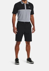 Pánské polo tričko Under Armour s černým vrškem a šedým středním panelem, doplněné černými šortkami a černými sportovními botami. Texturovaná, vlhkost-odvádějící tkanina.