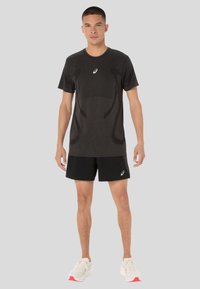 Black athletic T-shirt with short sleeves and a round neck, featuring textured accents and a subtle logo at the center, paired with black shorts.