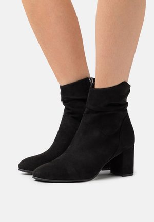 Stivaletti neri in suede alla caviglia con un design arricciato, punta quadrata e tacco spesso. Presentano una cerniera laterale per una facile vestibilità.