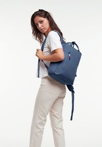 Mörkblå ryggsäck med rektangulär form, tillverkad av tyg; har justerbara remmar, en framficka med dragkedja och en färgglad accentdetalj.