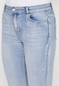 Light blue jeans with a slim fit, featuring a metal button, subtle whiskering, and minimal stitching details on pockets.
