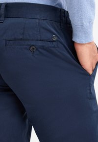 Navy blue trousers made from smooth fabric, featuring a back pocket with button closure, and a slightly tapered fit.