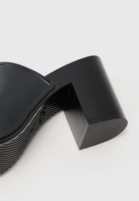 Sandal com salto alto preto, com bico arredondado e um salto em bloco retangular largo. Apresenta um cabedal liso e brilhante e um design de sola texturizado.