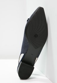 Zapato azul marino con parte superior de tela con topos y suela de goma negra. La suela presenta un diseño curvado para mayor agarre.