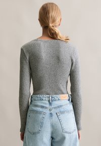 Woman with blonde hair tied in a ponytail wearing a gray ribbed sweater and light blue high-waisted denim jeans facing away.