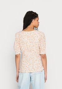 Blusa floral branca com flores laranja, mangas curtas bufantes e detalhe na cintura franzida, combinada com jeans azul claro.
