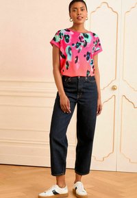 Krátky rukáv, jasne ružový top s leopardím vzorom; skombinovaný s vysokými tmavými džínsami a bielymi teniskami s námornícky modrými akcentmi.